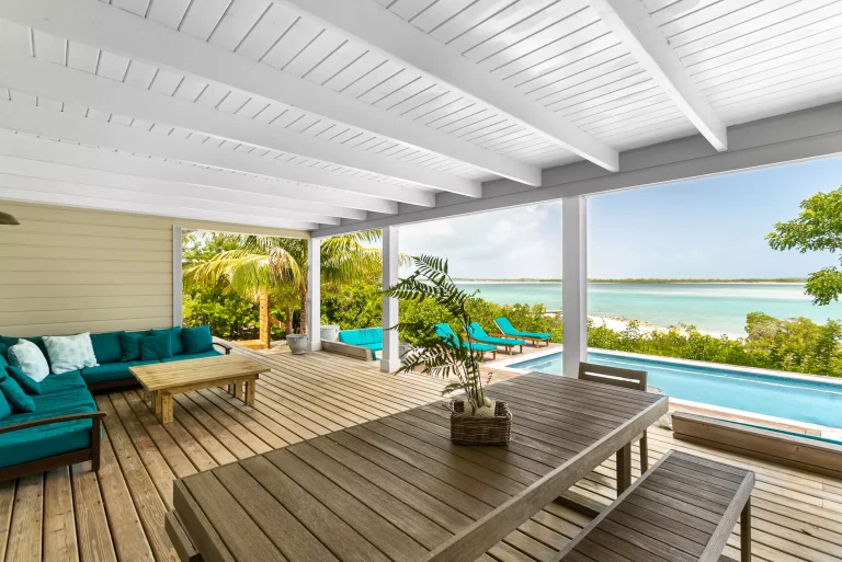 Covered deck with dining table and teal sofas at Sueno de Mar, George Town, Great Exuma